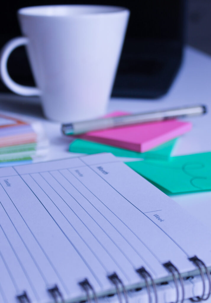 Taustakuva, jossa kuvituskuvana työpöydän tarvikkeita, kuten post-it-lehtiö, kynä, kalenteri ja kahvikuppi.